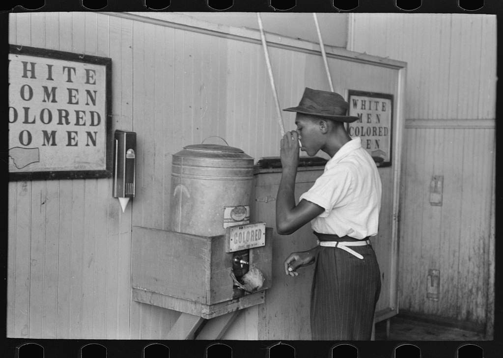 Man drinking from a "Colored" water cooler at a streetcar terminal, Oklahoma City, 1939
